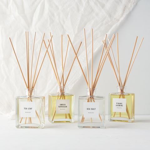 Assorted Makana reed diffusers with muted lighting and gauzy white backdrop