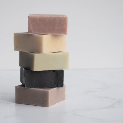 Makana Botanical Bar Soaps in various scents stacked on white marble background