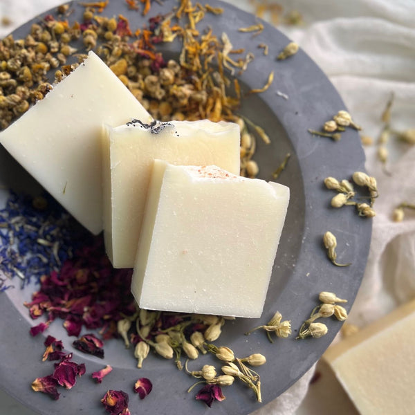 Handcrafted soap bars on dried flowers and botanicals in a rustic grey concrete bowl